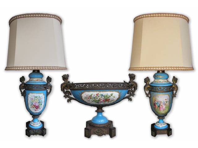 Sèvres - Maravilhoso conjunto com três peças, par de abajur e centro de mesa em porcelana na cor azul royal. Bases ricamente ornamentadas com ramalhetes de flores em bronze cinzelado e repuxado. Par de alças laterais com figuras femininas, varandas vazadas e desenhos de flores em alto-relevo. Peças finamente decoradas ao centro, em ambos os lados, com variação de temas palacianos e ramalhetes de flores, estes, também decorando toda a parte interna do centro de mesa. Peças sem detalhes nem restauros, para colecionadores. - França, séc. XIX/XX