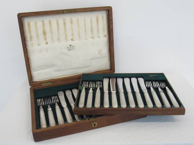 Mappin & Webb Ltd. - Faqueiro para peixe em metal espessurado a prata composto de doze garfos e doze facas para peixe, com cabos ornados em frisos estriados, acompanha estojo de madeira forrado com veludo verde, tampa decorada com reserva de bronze com formato de escudo, 35 x 26 x 6 cm.