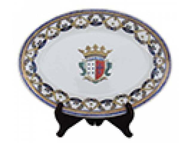 Travessa oval em porc. vitrificada decor. em policromia motivo heráldico contendo, ao centro brasão de armas encimado por coroa de conde, ladeado por barrado ornado com guirlandas e laçarotes, e cercaduras frisadas. c = 30,5 cm h = 22 cm. Europa, transição dos séculos XIX e XX.