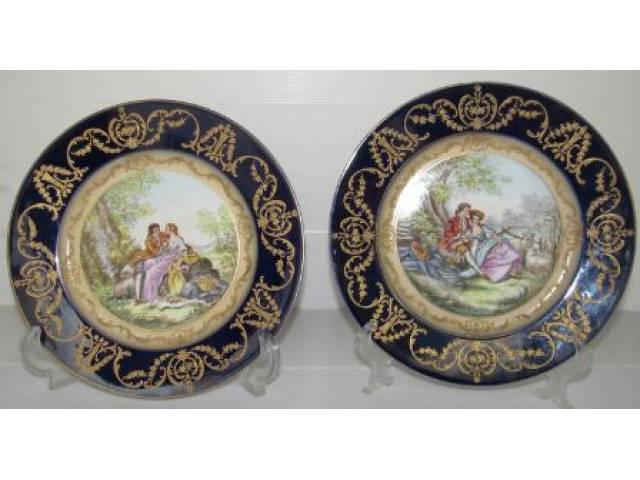 Sévres - Par de antigos pratos em porcelana, esmaltados ao centro, casal em cena romântica no campo, borda faixa azul cobalto ornamentada com fino rendado alto relevo em folha de ouro, assinado na frente e timbrado no verso, D = 25 cm - França séc. XIX/XX obs: um dos pratos apresenta pequeno desgaste na lateral do verso e timbre apagado por provável restauro - França