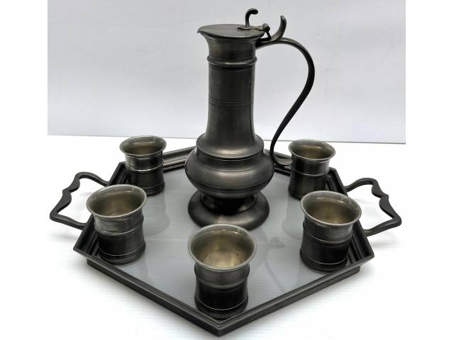 Serviço com jarra e 6 copos em estanho com bandeja de vidro e alça em estanho.