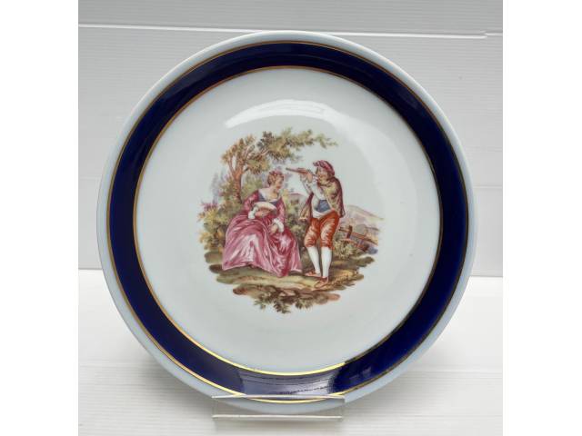 Prato decorativo em porcelana representando cenas de  flautista e dama ao centro , bordas ricamente ornamentadas na cor azul cobalto e filete dourado .Diâm. 24cm